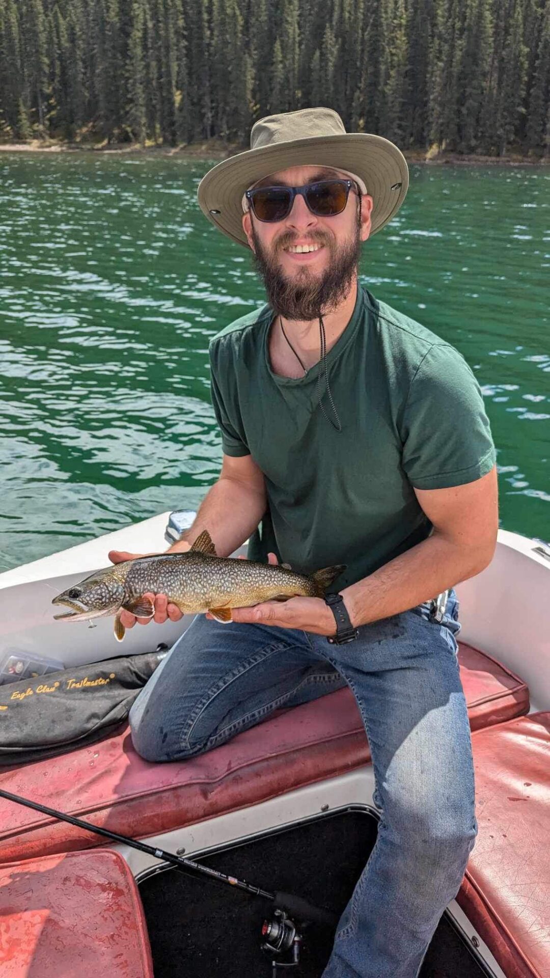 A lake trout held up over the jade-green water of Rock Lake